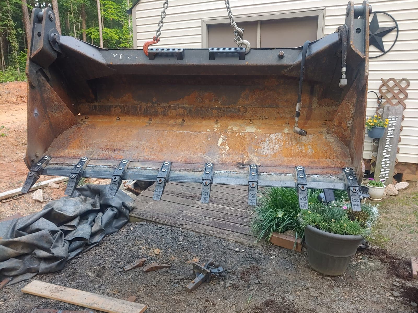 A loader bucket slung from chains with a new bolt-on tooth bar and shanks fitted along the cutting edge.