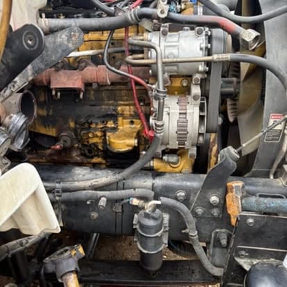 A yellow Caterpillar engine in the chassis with the alternator, fan drive and coolant lines exposed.