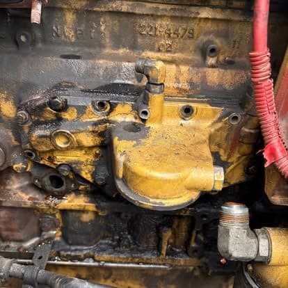 Casting numbers stamped into the side of a yellow Caterpillar engine block with the oil cooler housing removed.