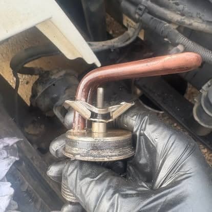A gloved hand holding a bent copper line and wing-nut fitting removed from a machine.