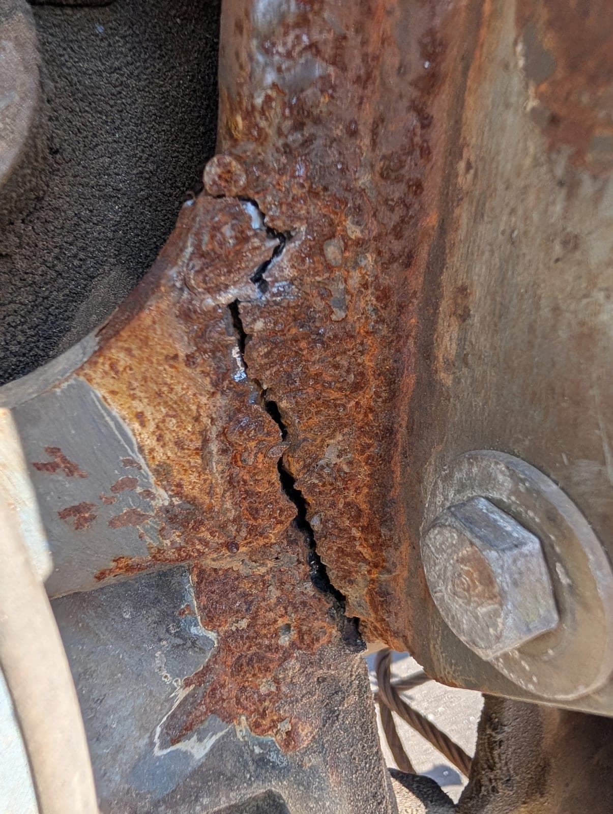 A crack running through a heavily rusted steel bracket and frame member, photographed before the repair.
