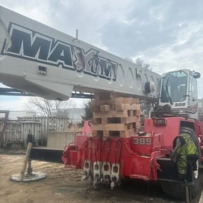 The boom of a red Maxim rough terrain crane resting on stacked timber cribbing during hydraulic service.