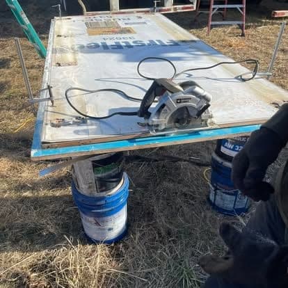A circular saw sitting on a trailer side panel laid across buckets, mid-way through cutting the replacement section.