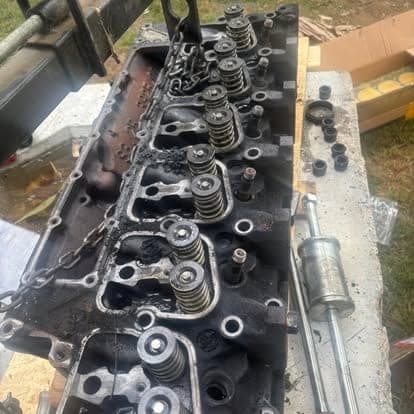 A carbon-caked cylinder head during teardown, valves and springs still in place, parts laid out alongside.