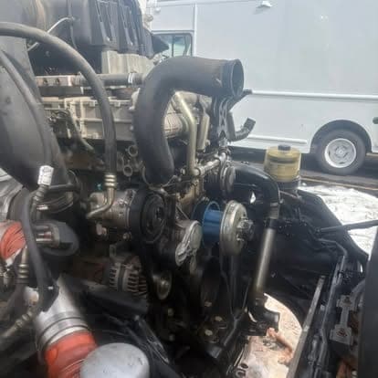 The front of a diesel engine showing the belt drive, alternator and power steering reservoir during a repair.