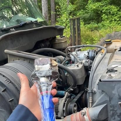 A mechanic holding a replacement filter element beside the open engine bay of a truck on a wooded jobsite.