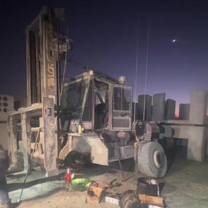 A fire-damaged heavy forklift standing in a concrete yard at dusk, awaiting assessment.