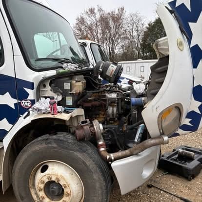 A white Freightliner M2 box truck with the hood tilted open, engine and turbo exposed for service.