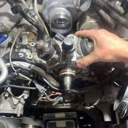 A mechanic's hand seating a high-pressure fuel injector into the cylinder head next to the turbocharger.
