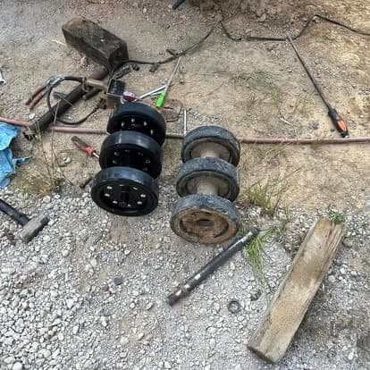 Wheel hubs, brake drums and an axle shaft laid out on the gravel during a brake and bearing job.