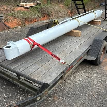 A large hydraulic cylinder strapped down to a flatbed trailer for transport back to the shop.