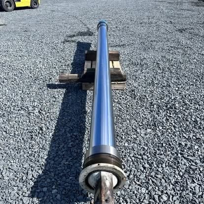 The polished chrome rod of a large hydraulic cylinder resting on a pallet on the gravel yard.