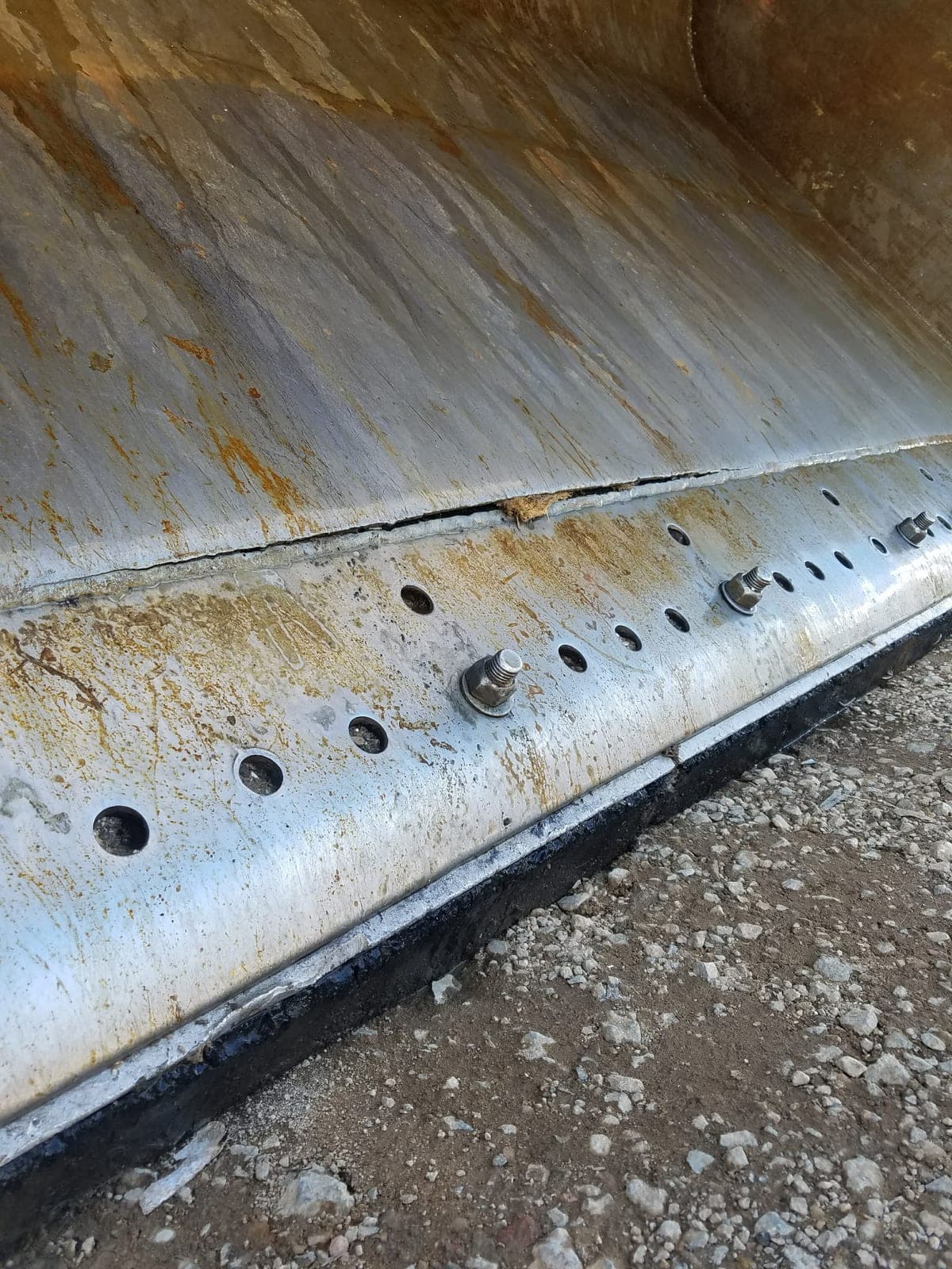 A new cutting edge welded and bolted along the bottom of a bucket, countersunk bolt holes running its length.