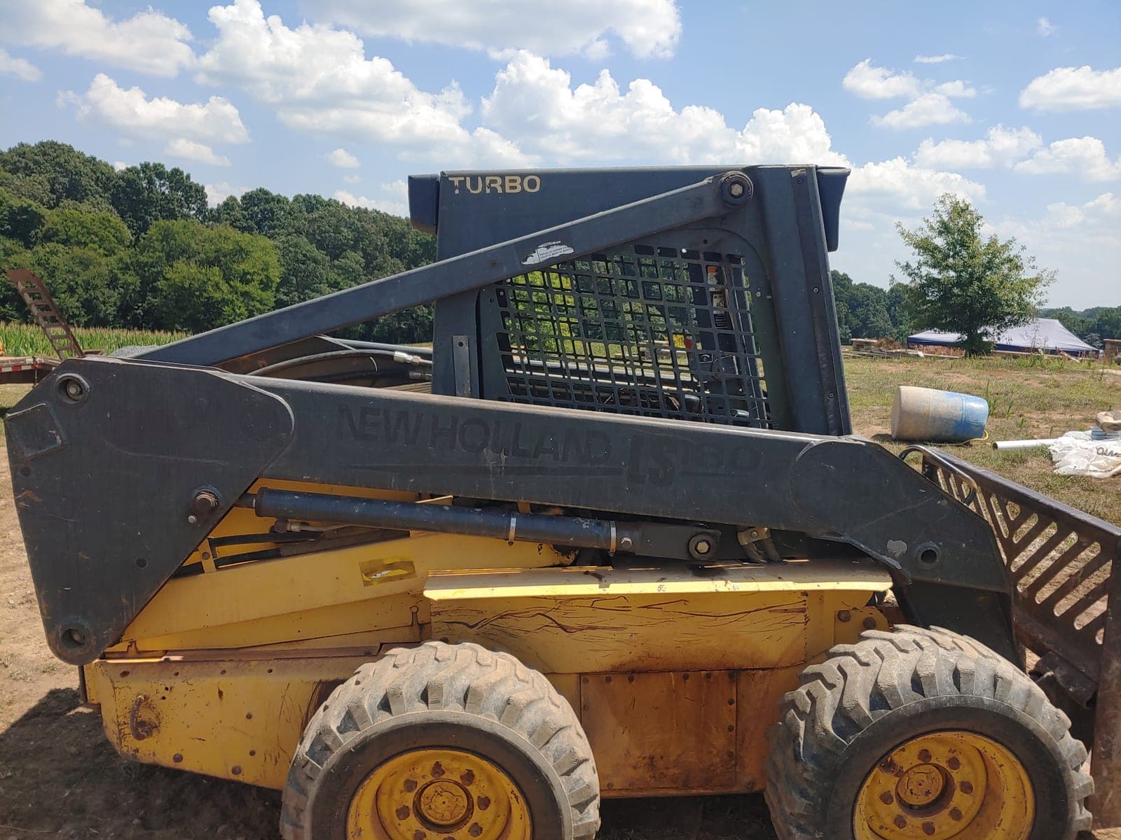A New Holland LS180 Turbo skid steer loader parked in a field with its loader arms down.