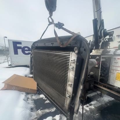 A radiator and charge air cooler assembly lifted out by the service truck crane on a snowy yard.