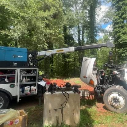 The service truck crane extended over a truck with the hood and front axle pulled apart during an on-site repair in the woods.