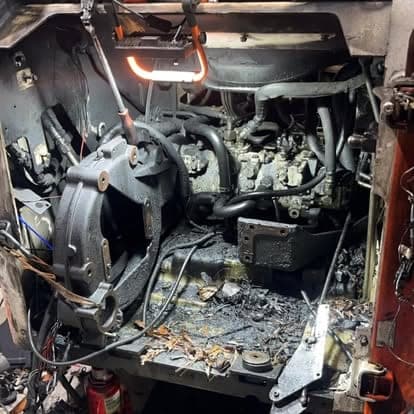 The stripped engine compartment of a skid steer loader lit by a work light, with the engine removed for repair.