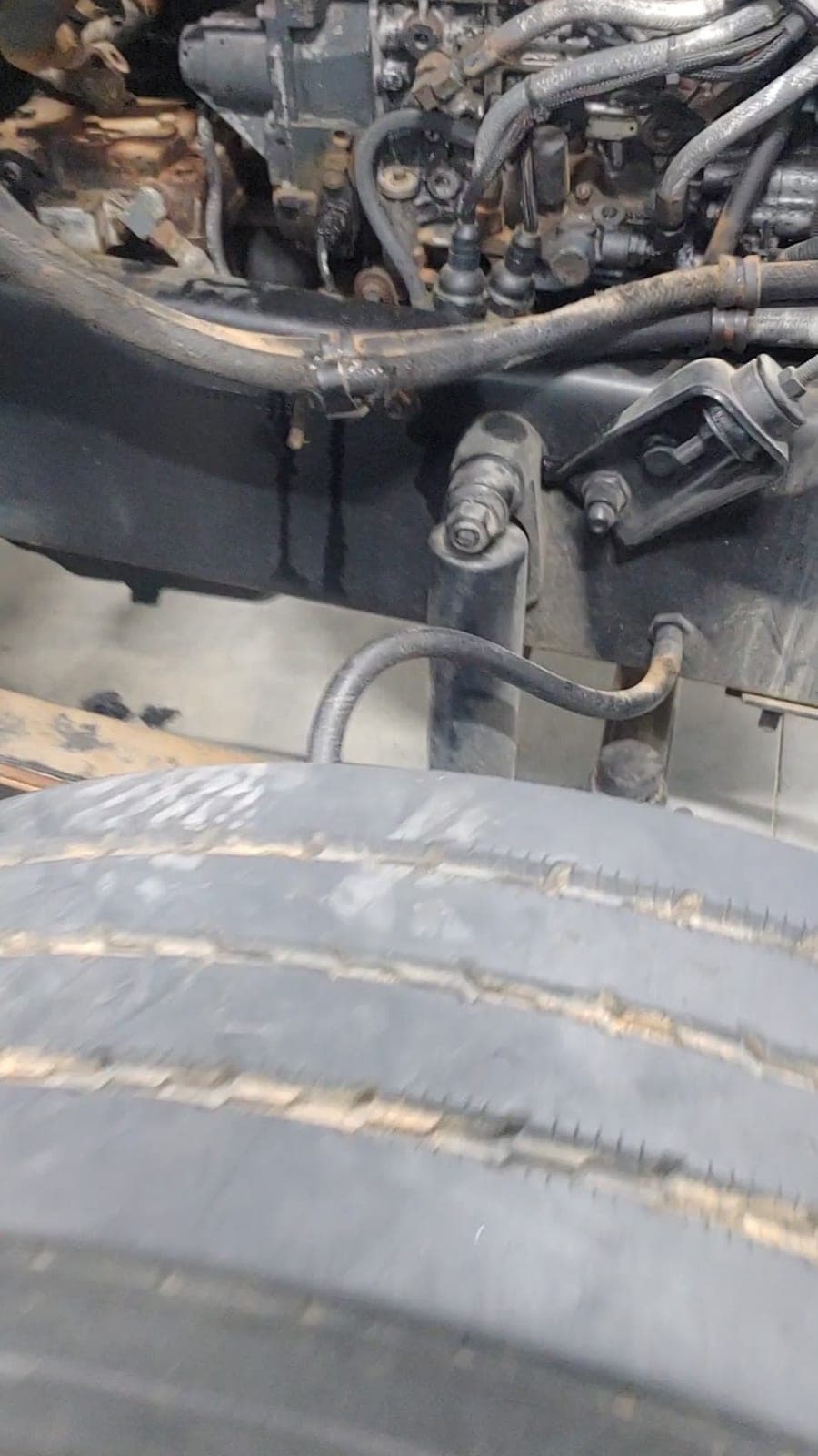 A view across the steer tire into the engine bay and frame rail of a truck up in the shop.