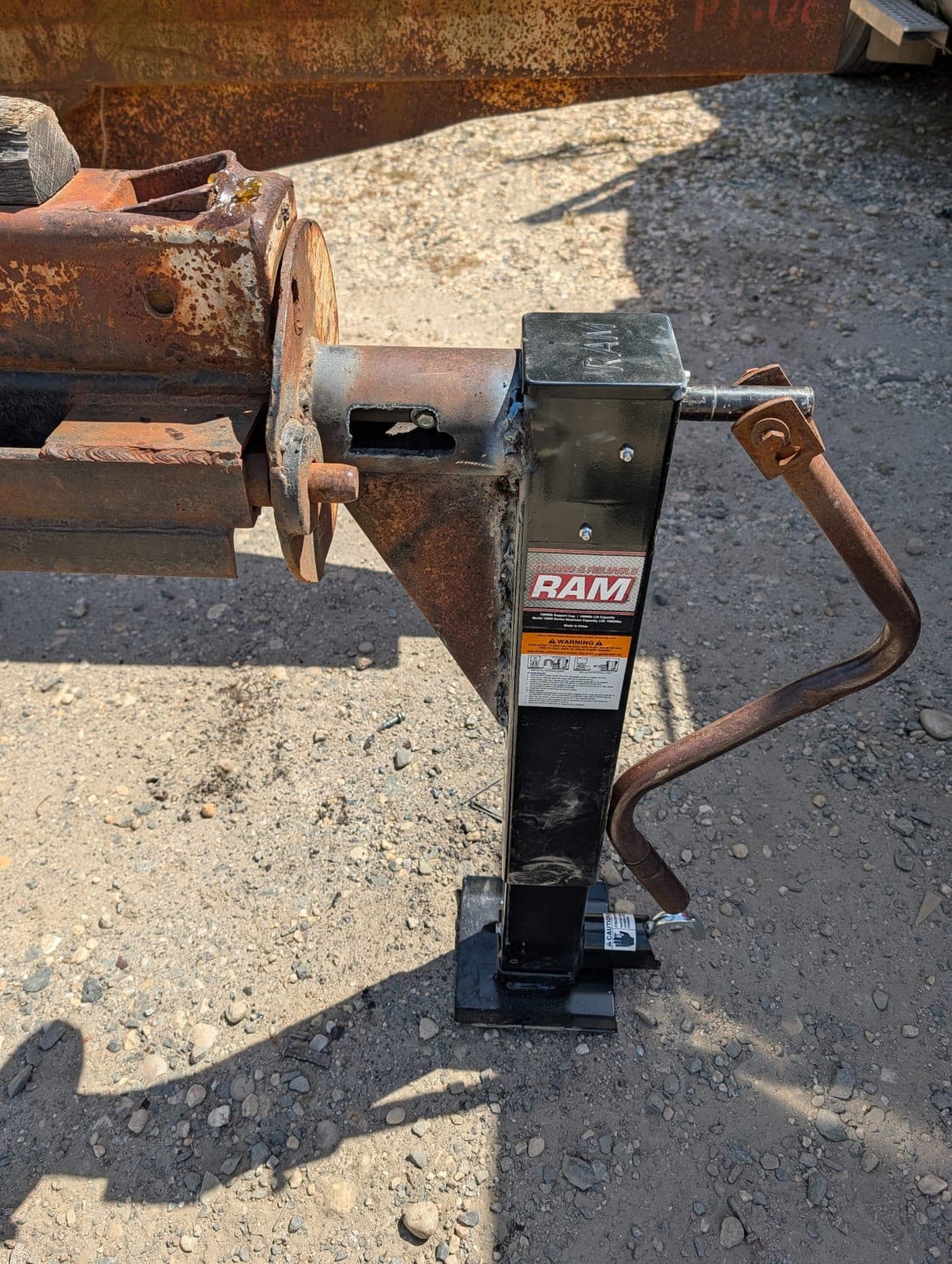 A new drop-leg jack welded onto the rusted tongue of a trailer, standing on the gravel.