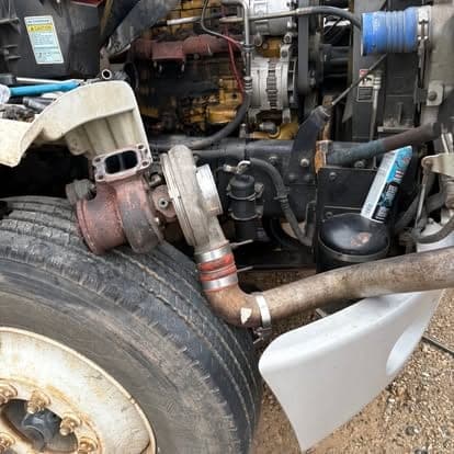The turbocharger and exhaust elbow on a Caterpillar engine, viewed past the front wheel of the truck.