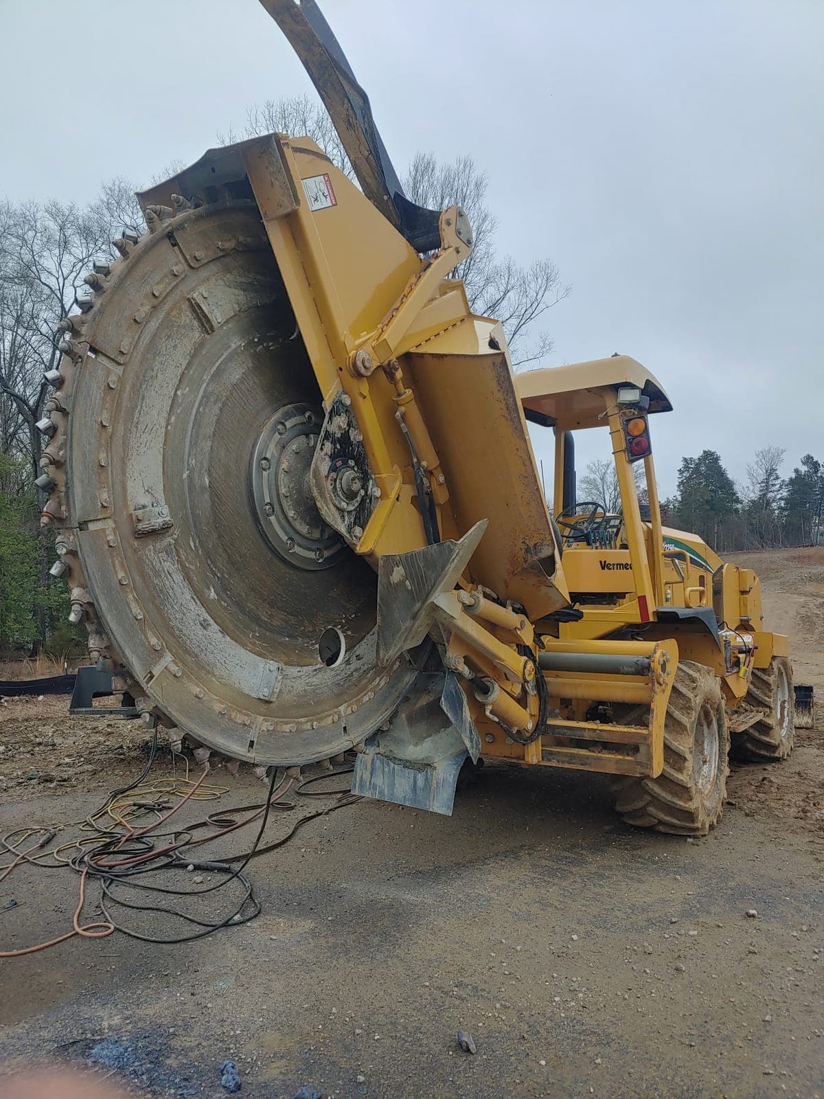 A Vermeer trencher with its carbide-toothed rock wheel raised and welding leads run out across the ground for an on-site repair.