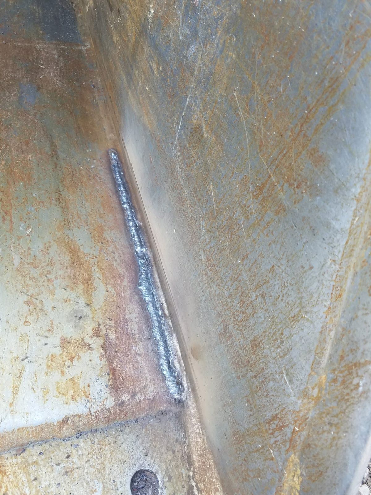A close-up of a stacked weld bead running down a corner joint in heavy steel plate.